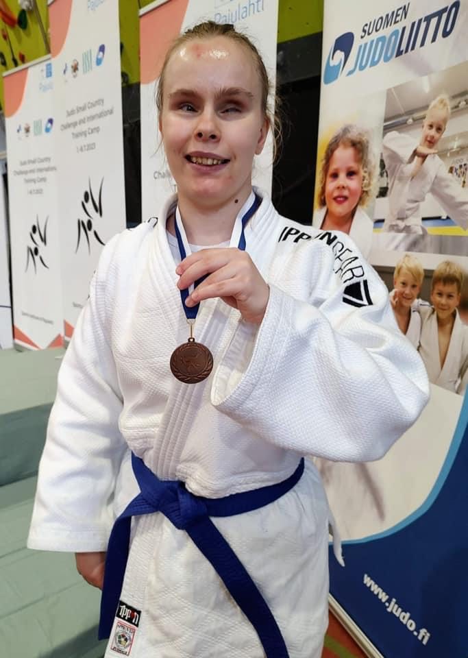 Tessa Koponen esittelee palkintoaan, hänellä on valkoinen, sinisellä vyöllä kietaistu puku. Ilme kertoo onnistumisesta!